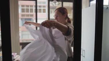 Çamaşır odasında beyaz bir çarşafı katlayan kadın.