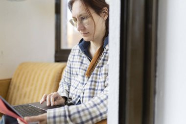 Uzaktan kumandayla çalışan, kitap okuyan, koltukta rahatça oturan serbest çalışan bir kadın.
