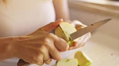 Tahta kesme tahtasının üzerinde yeşil bir elmayı kesen kadın elleri.