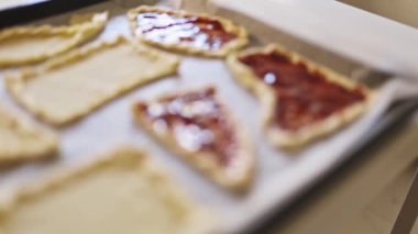 Elleri hamur parçalarına kırmızı meyve reçeli yayıyor.