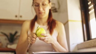 Kızıl saçlı kadın küçük bir bıçakla yeşil bir elmayı soyuyordu.