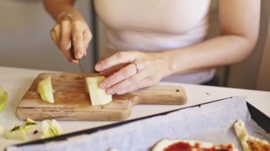Kadın ahşap kesim tahtasındaki yeşil elmaları dilimliyor. Meyve pizzası hazırlıyor.