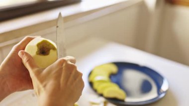 Kadın mutfak tezgahında bıçakla elmayı dikkatlice soyuyor.