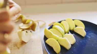 Yeşil elmaları soyan ve dilimleyen eller, onları mavi bir tabakta düzenliyor.