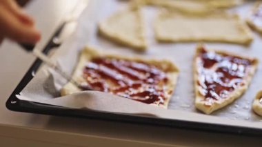 Elleri hamurun üzerine çilek reçeli serpiştiriyor.