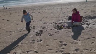 Okyanusun yakınındaki kumlu bir sahilde oynayan iki çocuk.