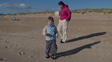 Anne ve oğlu güneşli bir sahilde sakin bir yürüyüşün tadını çıkarıyorlar.