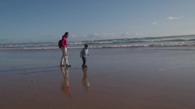 Baba ve oğul, güzel bir kumsalın ıslak kumu boyunca keyifle yürüyorlar.