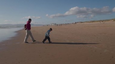 Anne ve oğlu sahilde koşuyor, eğleniyorlar.