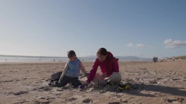 Anne ve oğul güneşli sahilde kumdan kaleler inşa ediyorlar.
