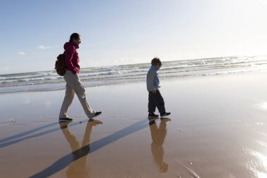 Anne ve oğlu sahilde huzurlu bir yürüyüşün tadını çıkarıyor, birlikte kalıcı anılar yaratıyorlar.