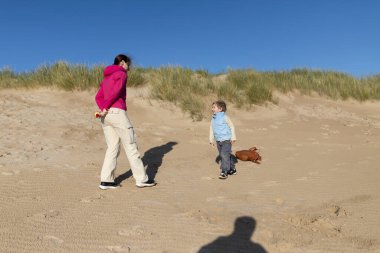 Anne ve oğlu kumulların yakınındaki kumsalda güneşli bir günün tadını çıkarıyorlar.