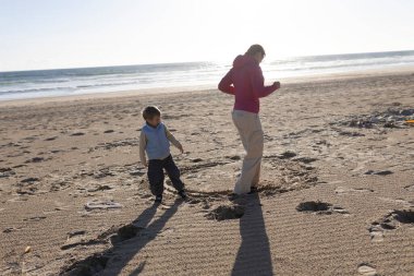 Anne ve oğlu gün batımında sahilde neşeli bir anın tadını çıkarıyorlar.