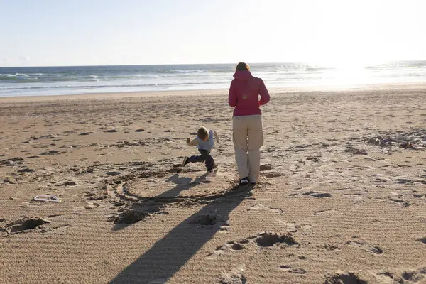 Anne ve oğlu gün batımında kumsalda çember çiziyor.