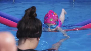 Genç kız kapalı havuzda eğitmenle yüzmeyi öğreniyor.