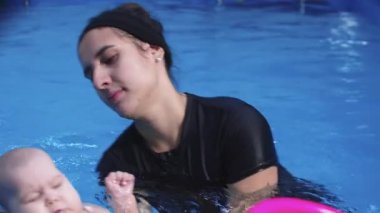 Eğitmen yüzme dersleri sırasında bebeğe bakıyor, erken gelişimi ve su güvenini teşvik ediyor