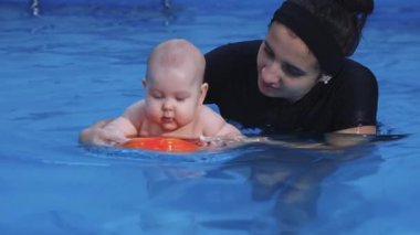 Bebek yüzme dersi sırasında bebeğe havuzda yardımcı oluyor.