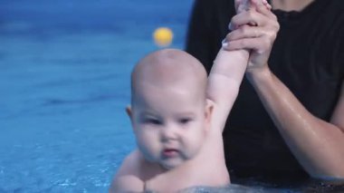 Eğitmen bir bebeğe kapalı havuzda yüzmeyi öğretiyor.