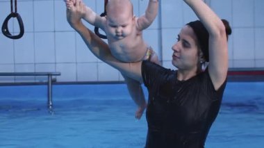 Eğitmenler bebek yüzme dersleri sırasında bebeği suyun üstünde tutuyorlar.