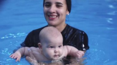 Bir bebeğe havuzda yüzmeyi öğretirken kucağında bir bebek tutan uzman eğitmen.
