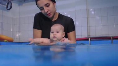 Eğitmen, havuzda yüzen bebeğe yardım ediyor.