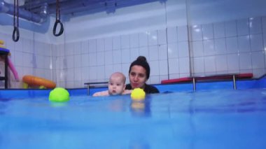 Kapalı havuzda yüzme dersi sırasında eğitmen bebeğe yardım ediyor.