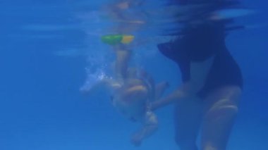 Eğitmen sevimli bir bebeğe kapalı havuzda yüzmeyi öğretiyor.