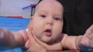 Nitelikli eğitmenler bir bebeğe kapalı havuzda yüzmeyi ve yüzmeyi öğretiyor.