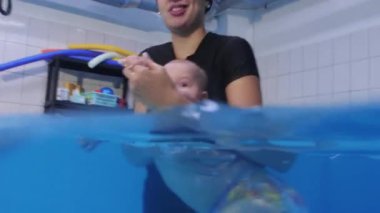 Yüzme hocası havuzda yüzen bir bebeği tutuyor, ona yüzmeyi öğretiyor.