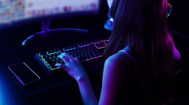 Oyuncu kız, maçtan önce neon bilgisayarının başında ellerini gevşetiyor. Orta çekim