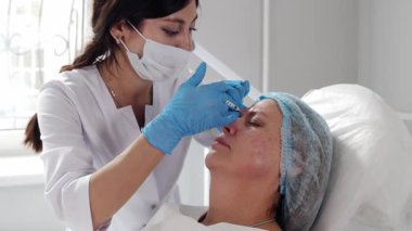 Kozmetik uzmanı olgun kadınların yüzüne yaşlanma önleyici iğne yapıyor.