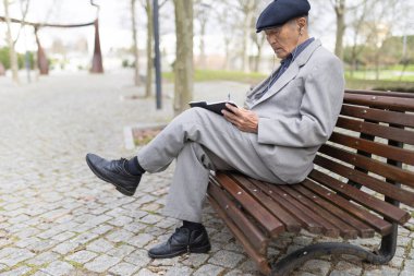 Kıdemli işadamı, şehir parkında kulaklıklarıyla müzik dinlerken defterine notlar alıyor.