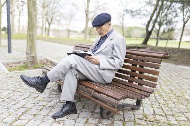 Kulaklık takan kıdemli bir adam parkta bankta otururken defterine not alıyor.
