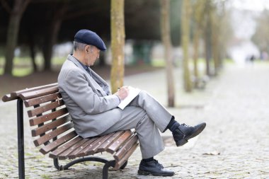 Yaşlı bir adam bankta kulaklıkla müzik dinlerken deftere notlar alıyor.