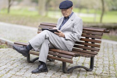 Park bankında otururken deftere yazı yazan kıdemli yazar, huzurlu bir ortamın tadını çıkarıyor.