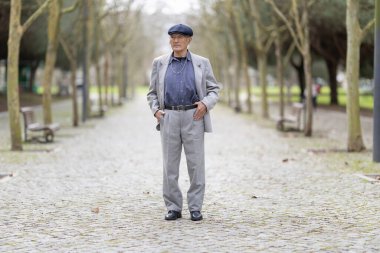 Bir park yolunda elleri ceplerinde duran zarif yaşlı bir adam.