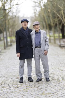 Yetişkin oğlu, parkta birlikte yürürken, aile bağlarını ve bakıcılıklarını gösteren yaşlı babasına destek oluyor.