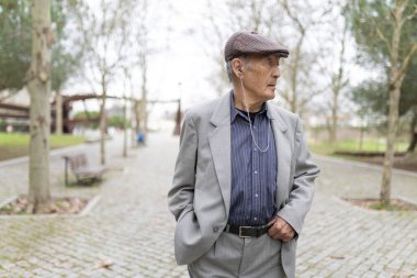 Huzurlu bir park ortamında rahatlatıcı bir yürüyüş sırasında müziğin tadını çıkaran kıdemli bir adam.