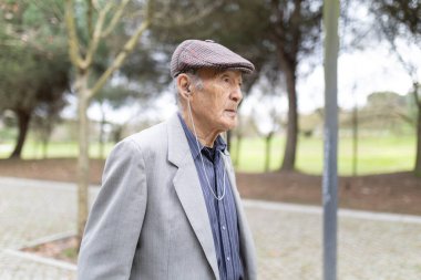 Yeşil bir parkta rahatlatıcı bir yürüyüş sırasında kulaklık takan ve müziğin keyfini çıkaran son sınıf öğrencisi.