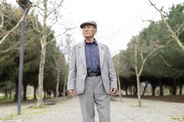 Kıdemli Asyalı takım elbiseli ve gazeteci şapkalı bir adam parkta rahatça geziniyor.