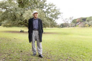 Huzurlu bir parkta durmuş, temiz havanın ve doğanın sükunetinin tadını çıkarıyor.