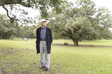 Huzurlu bir parkta duran yaşlı adam, temiz havanın ve sükunetin tadını çıkarıyor.