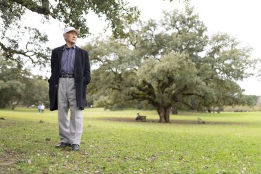Huzurlu bir parkta durmuş, doğanın huzurunu kucaklayan yaşlı bir adam.