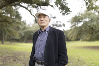 Yaşlı Asyalı adam yeşil bir parkta kulaklık takıyor ve müzik dinliyor.