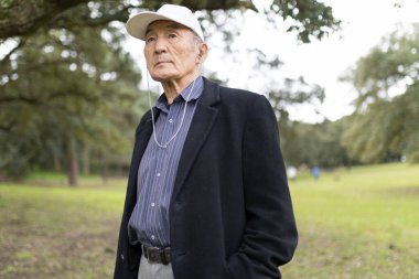 Huzurlu bir park ortamında müziği seven, sükunet ve rahatlığı kucaklayan kıdemli Asyalı bir adam.