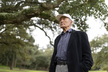 Yaşlı Asyalı adam, parkta yürürken kulaklıkla müzik dinliyor, emekliliğin tadını çıkarıyor.