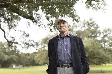 Şapka takan ve kulaklık takan yaşlı bir adam parkta müzik dinliyor.