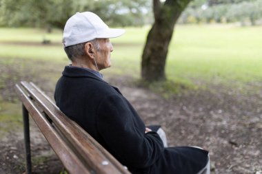Huzurlu bir parkta bankta otururken müzik dinleyen kulaklık takan son sınıf öğrencisi.