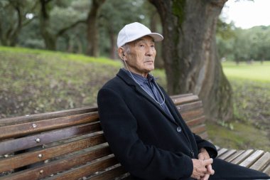 Yaşlı bir adam doğada müzikten zevk alıyor, bir bankta oturuyor.