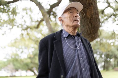 Kıdemli Asyalı adam, emeklilik yıllarını kucaklayarak, parkta rahatça yürürken kulaklıkla müzik dinliyor.